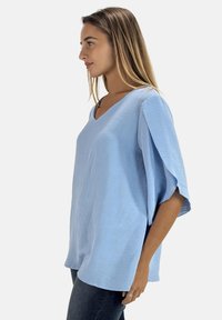 Top azul claro con escote en v y mangas cortas y anchas. Hecho de una tela texturizada, tiene un ajuste holgado y cae por debajo de las caderas.