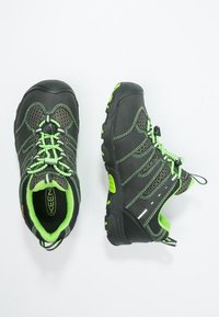 Mustat ja vihreät vaellusjalkineet, joissa on verkkopaneelit, nopea nauhakiinnitys, kestävä grip-pohja ja heijastavat yksityiskohdat näkyvyyden parantamiseksi.