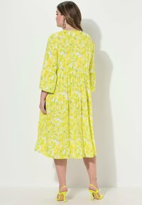 Sukienka w kwiatowy wzór w jasnym żółtym i białym kolorze, o długości do połowy łydki z rękawami do łokcia, z taliowanym pasem, w połączeniu z dopasowanymi żółtymi szpilkami.