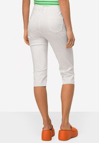 Witte capri-broeken met een elastische tailleband, voorzien van twee achterzakken en een elegante, gladde textuur, gecombineerd met oranje platform schoenen.