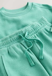 Detailný záber na svetlo tyrkysový pruhovaný pletený svetrový úplet a zodpovedajúce teplákové nohavice s elastickým pásom a sťahovacou šnúrkou.