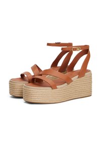 Brown leather wedge sandals with woven rope soles, featuring crisscross straps, ankle adjustment, and a smooth footbed.