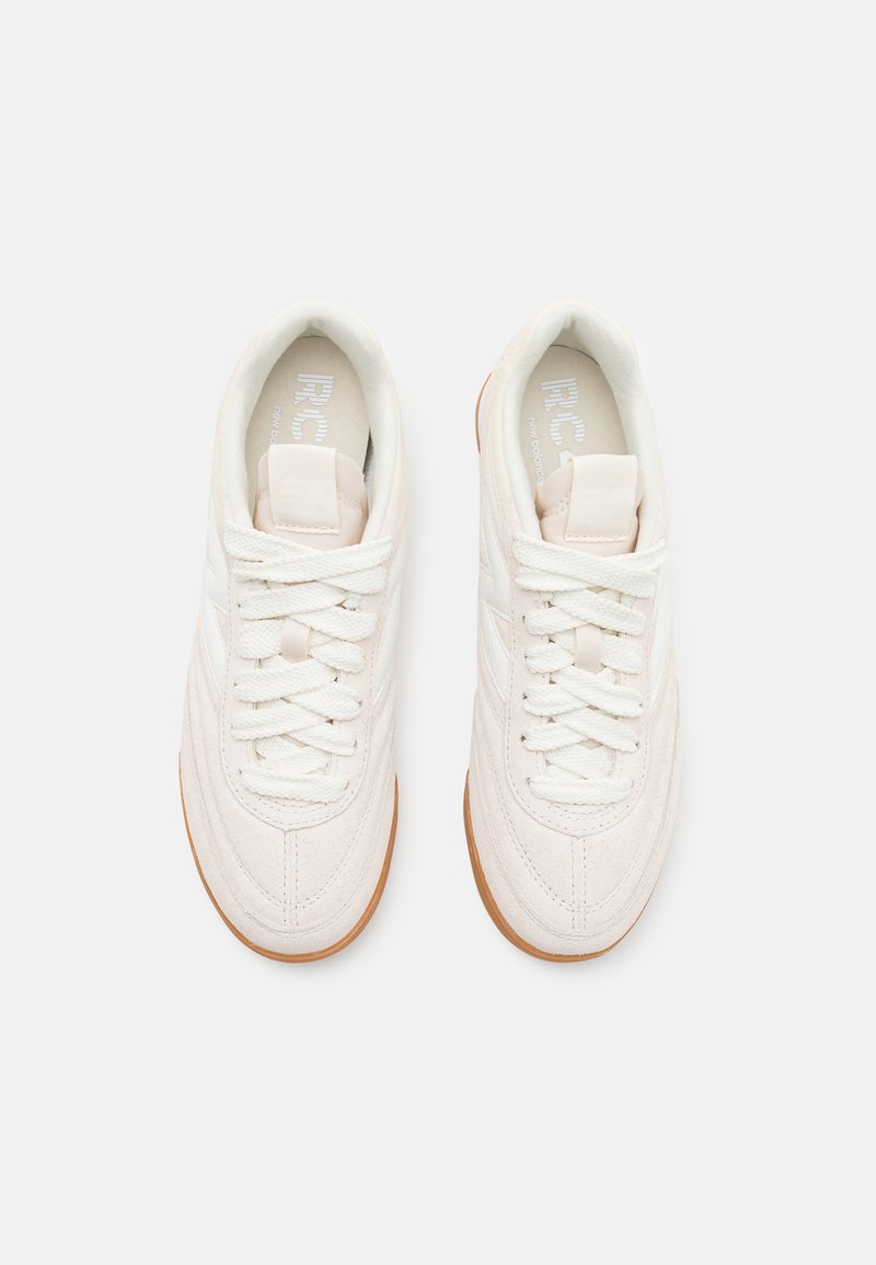 Baskets en daim blanc avec une surface texturée, bout rond, lacets plats et semelle en caoutchouc brun clair. Design minimaliste avec des accents sur les côtés.
