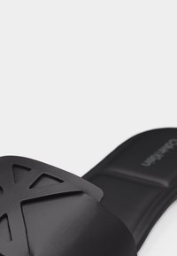 Sandale noire à talon avec un design géométrique découpé sur la bride et une semelle intérieure rembourrée, marquée Calvin Klein visible.