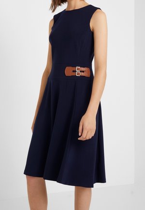 Robe sans manches bleu marine avec corsage ajusté, jupe évasée et ceinture marron à double boucle à la taille.