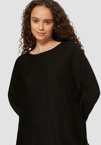 Zwarte oversized trui, met textuur gebreid, wijde halslijn, lange mouwen, relaxte pasvorm, met labeldetail aan de onderzijde rechts.