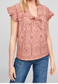 Blusa di cotone rosa con ricami ad occhio di fiore, maniche corte con volant e scollatura con nodo. Abbinata a jeans in denim blu.