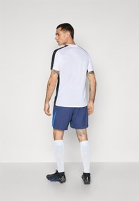 Îmbrăcăminte sportivă compusă dintr-un tricou scurt alb și negru și pantaloni scurți albaștri cu un accent albăstrui contrastant, asortați cu ghete negre și șosete albe.