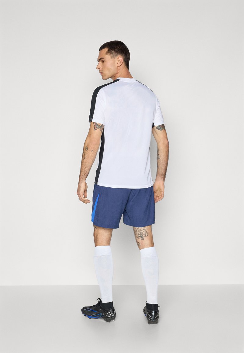 Îmbrăcăminte sportivă compusă dintr-un tricou scurt alb și negru și pantaloni scurți albaștri cu un accent albăstrui contrastant, asortați cu ghete negre și șosete albe.