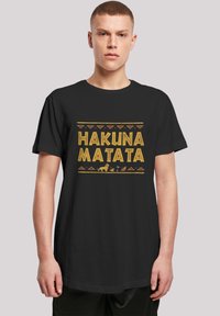 Melna kokvilnas T-krekls ar uzrakstu "HAKUNA MATATA" dzeltenā krāsā, rotāts ar cilšu rakstiem un dzīvnieku siluetiem dzīvās krāsās.
