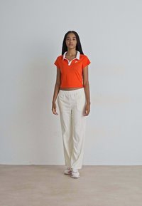 Oranje cropped polo shirt met witte kraag, gecombineerd met lichtbeige wijde broek en witte sneakers. Gladde, casual stof.