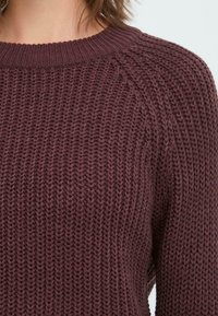 Maglione lavorato a maglia color bordeaux con un motivo testurizzato, colletto rotondo a costine e maniche raglan, che mette in mostra un tessuto spesso e accogliente.