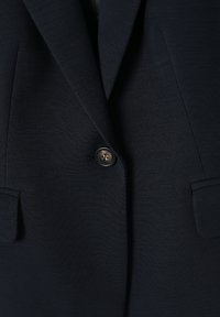 Blazer bleu marine foncé à bouton unique avec revers crantés et poches à rabat, fabriqué en tissu lisse et structuré.