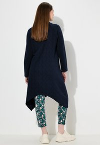 Tunic della marina con sottile motivo fogliare, orlo asimmetrico, abbinata a leggings fantasia in teal, con disegni di animali, e sneakers bianche.