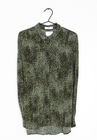 Blusa verde con estampado de serpiente, fabricada en tejido ligero, con cuello y mangas largas, y un dobladillo inferior ligeramente transparente.
