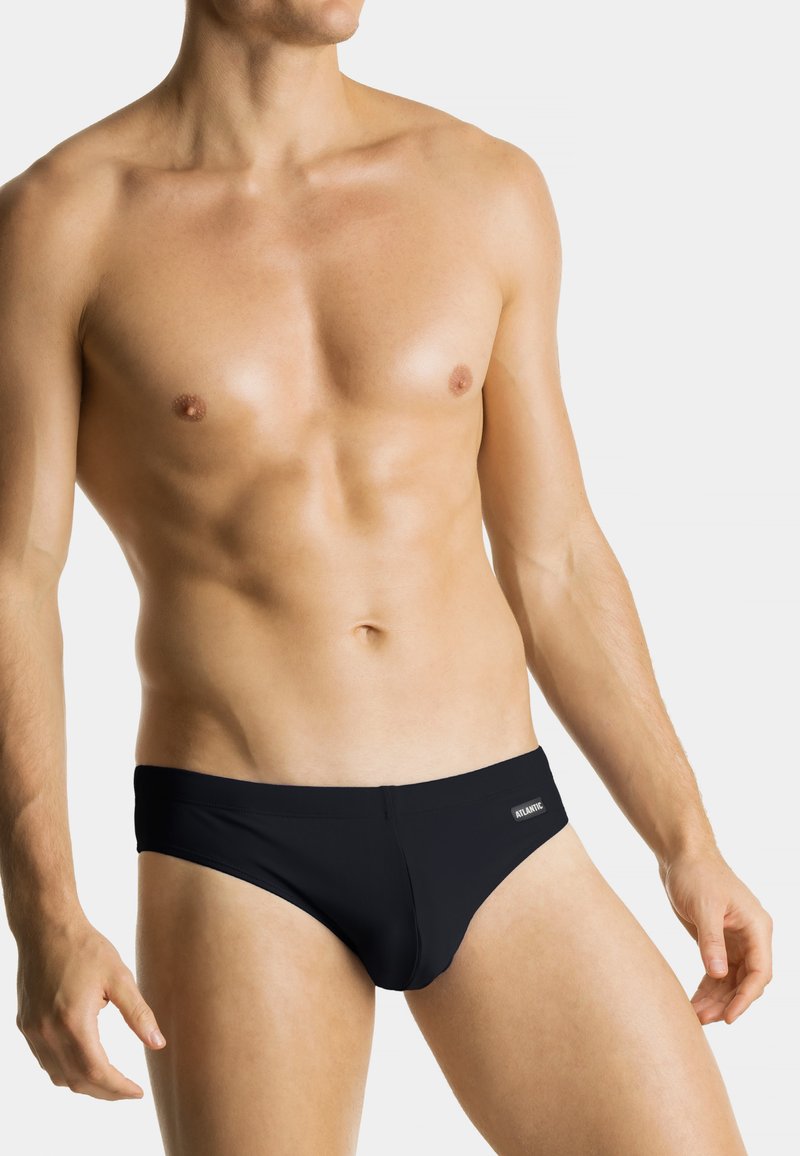 Czarne slipy kąpielowe wykonane z miękkiego materiału, charakteryzujące się dopasowanym krojem, niskim stanem i małą metką marki z przodu. Gładka faktura.