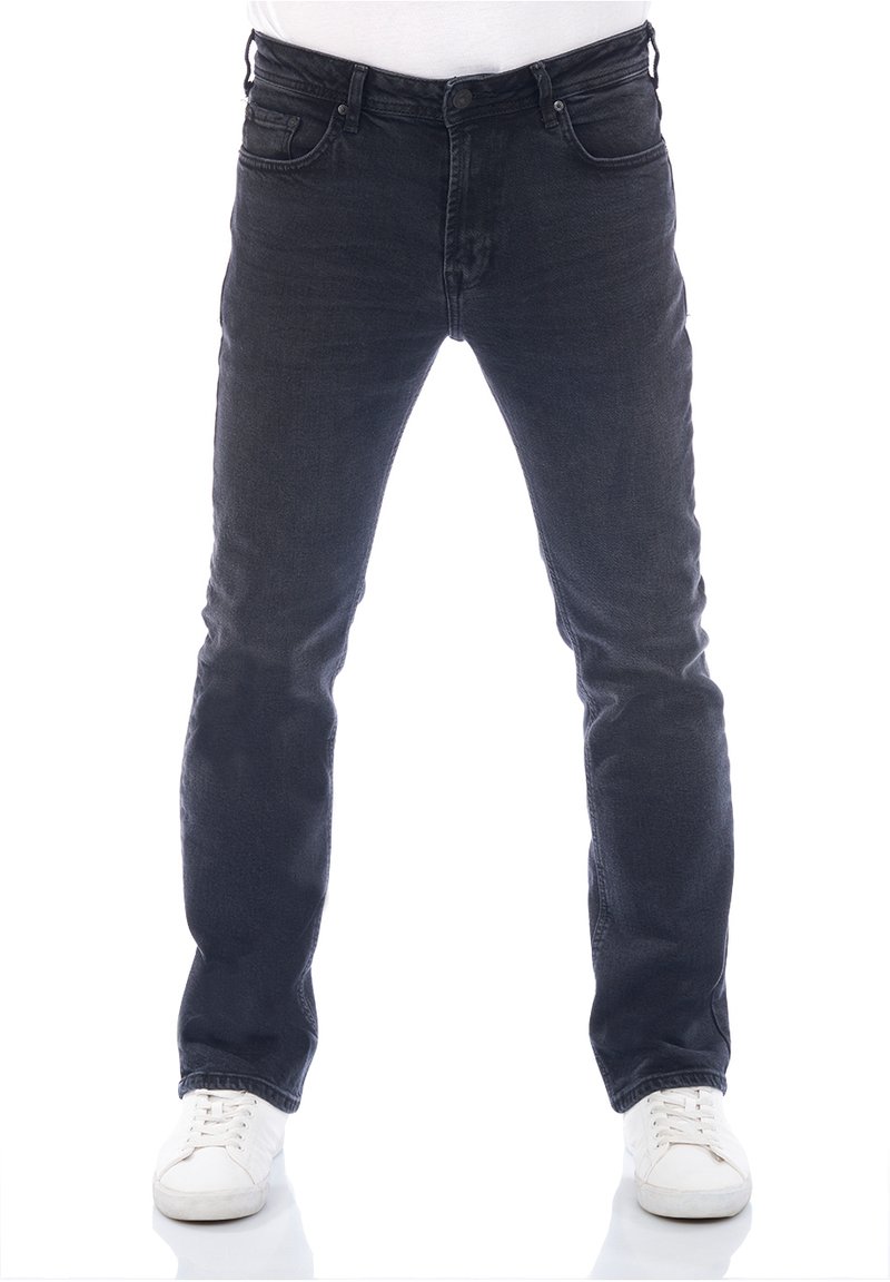 Jeans de mezclilla oscura con un corte slim, diseño de cinco bolsillos y cierre de botón. Llevados con zapatillas blancas, destacando colores contrastantes.
