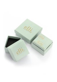 Hellgrüner quadratischer Kasten mit goldener Bedruckung, enthält einen offenen Kasten, der ein schwarzes Innere offenbart. Enthält Marken- und Produktionsdetails an der Seite.