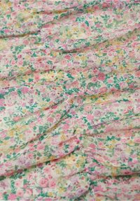 Gros plan sur un tissu plissé avec un petit imprimé floral multicolore en rose, jaune et vert sur un fond clair.