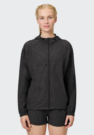 Schwarze, leichte Zip-Up-Jacke mit Kapuze, die ein dezentes, strukturiertes Muster aufweist, elastische Bündchen hat und einen lässigen Schnitt bietet. Kombiniert mit Shorts.