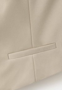 Tissu beige en gros plan montrant une poche fendue horizontale avec un détail de bande de tissu assortie sur un matériau cousu.