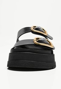 Des sandales noires à plateforme avec une finition en cuir lisse, dotées de deux accents de boucle en or et d'une semelle noire texturée.