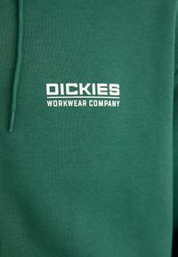 Groene sweatshirt van glad katoen, met een wit logo dat in het midden van de borst staat en "DICKIES WORKWEAR COMPANY" leest.