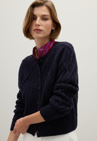Marinefarbener Strickcardigan mit rundem Halsausschnitt, langen Ärmeln und Knopfverschluss. Mit gerippten Bündchen und Saum, strukturiertem Stoff.