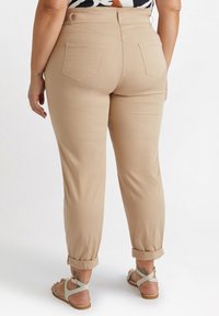 Beiga cropped byxor med uppvikta ärmar, har en mjuk textur, två bakfickor och en figurnära midja. Bärs med ljusa sandaler.