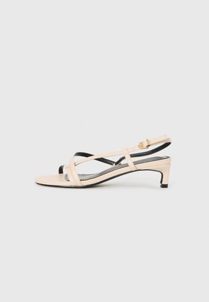 Beige Leder Slingback-Sandale mit überkreuzten Riemen, niedriger Ferse und schwarzen Akzenten. Glatte Textur und minimalistisches Design.
