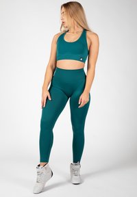 Teal sportbeha en high-waisted legging gemaakt van rekbare stof. De beha heeft een ronde halslijn en een logo-label; de leggings hebben een slim-fit pasvorm.