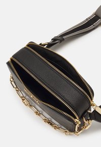 Schwarze Ledertasche mit goldenen Reißverschlüssen, einer Kettenakzent und einem gestreiften verstellbaren Tragegurt. Sie verfügt über mehrere Reißverschlussfächer.