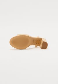 Sandal à talons hauts avec un dessus beige texturé, une semelle en caoutchouc marron et une fine sangle autour de la cheville. Présente des détails de marque subtils.