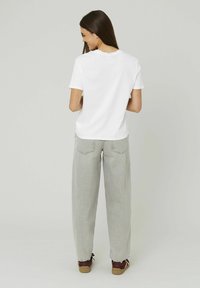 T-shirt en coton blanc avec un col rond, associé à un jean gris clair, ample, et des baskets marron, vu de dos.
