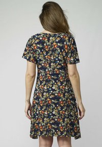 Kvinna med långt hår klädd i en marinblå klänning med korta ärmar och ett färgglatt blommönster, visad bakifrån.