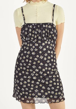 Robe noire à fleurs avec des marguerites blanches et des accents jaunes, featuring des fines bretelles, un corsage froncé et un ourlet festonné.