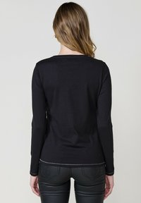 Must troo kuujo T-särk, millel on ümar kaelus, sile tekstuur ja kontrastsete õmbluste detailid alläärtes ja varrukates.