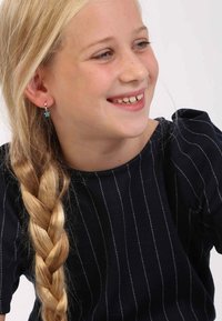 Kind met lang, blond gevlochten haar, gekleed in een donker top met witte verticale strepen en turkooise hangende oorbellen. Lachend gezicht.