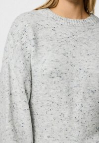 Pull en maille gris clair moucheté avec un col ras du cou côtelé, porté par une personne aux longs cheveux blonds.