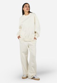 Felpa oversize color crema con polsini a coste, abbinata a pantaloni larghi coordinati. Presenta un tessuto morbido e un design minimalista.