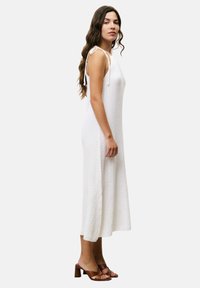 Weißes, ärmelloses Midi-Kleid aus strukturiertem Stoff, mit verstellbaren Bindeträgern und ausgestelltem Schnitt, kombiniert mit braunen Blockabsatzsandalen.
