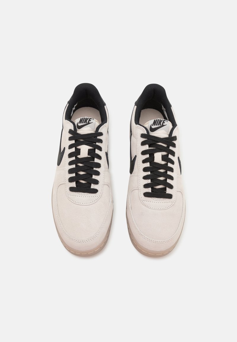 Sneakers bianchi in suede con lacci e dettagli neri, dotati di punta tonda, colletto imbottito e suola in gomma testurizzata color gomma.