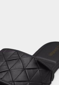 Μαύρο σανδάλι με λουράκι που έχει ανάγλυφο, ραμμένο γεωμετρικό σχέδιο και σβηστό πέλμα.