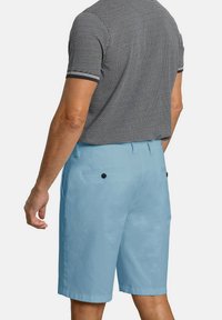 Pantalones cortos azul claro con una textura suave, dos bolsillos traseros con botones negros y un ajuste entallado, combinados con una polo a rayas en blanco y negro.