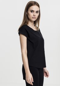 T-shirt noir à manches courtes en coton, avec un col rond et des poignets retroussés, au fit décontracté et à la silhouette droite.