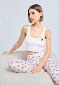 Débardeur blanc raccourci avec détail graphique de cerise, associé à un pantalon gris clair avec un motif de cerises. Texture douce, design décontracté.