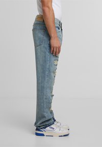 Jeans decolorate de un albastru deschis, cu un design drept, având detalii ruptă și o etichetă din piele la brâu. Asortați cu adidași albi.