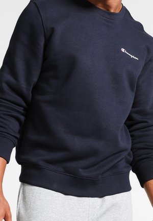 Granatowa bluza wykonana z miękkiej mieszanki bawełny, z okrągłym dekoltem i ściągaczami na rękawach. Małe białe i czerwone logo na piersi.