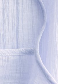 Gros plan sur un tissu bleu clair texturé avec une couture visible et un détail de bordure incurvé.