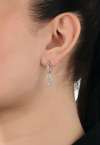 Orecchini a cerchio in argento con un charm a forma di cuore decorato con piccole cristalli trasparenti, appesi a un semplice gancio.